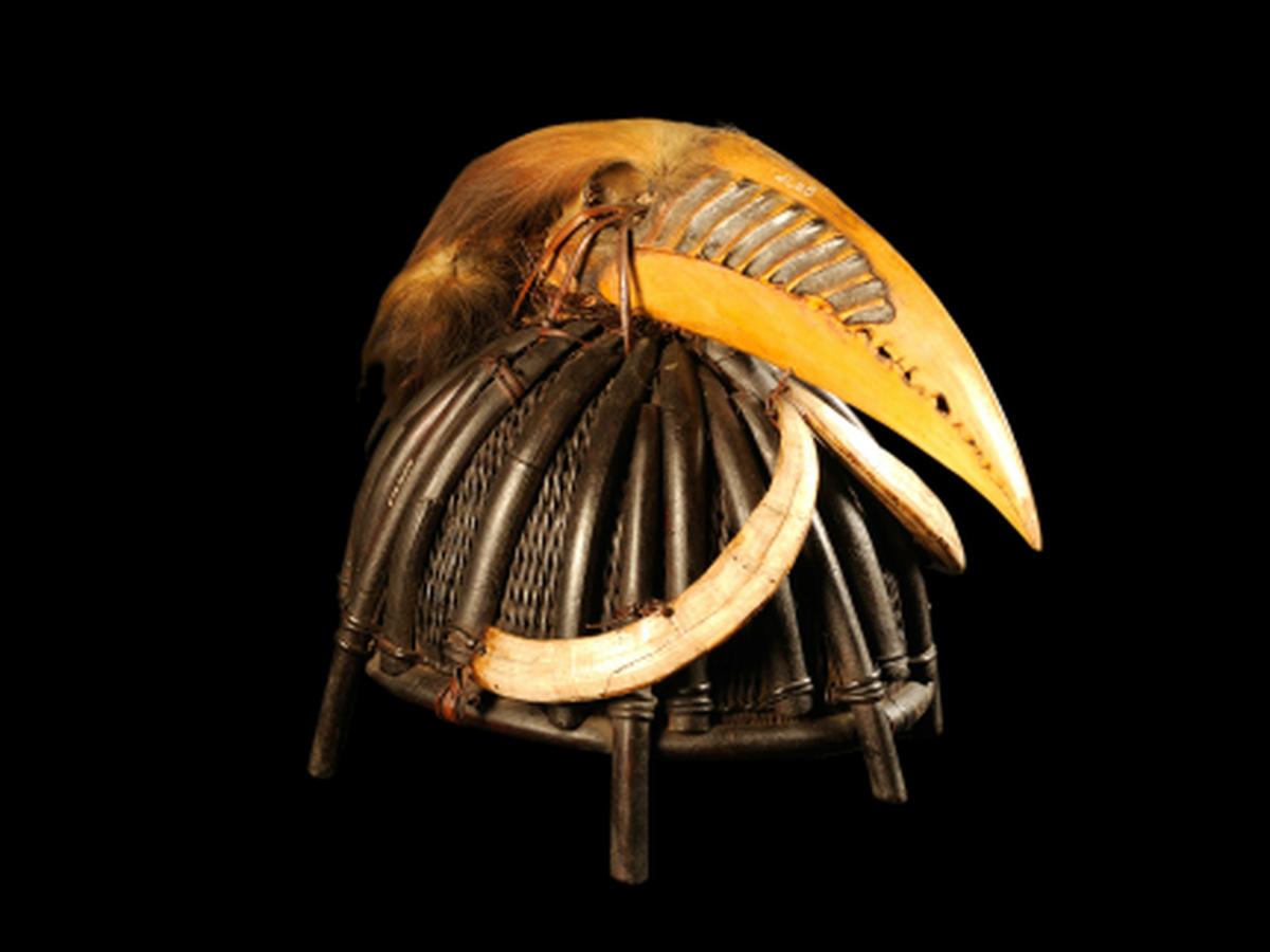 Dumlup-Lubra is a ceremonial as well as a functional helmet jointed to the Adi tribe of Arunachal Pradesh and displays its fine craft as well as the warrior tradition of that tribe. The oval-shaped helmet is made up of split, thick cane strips which are finely arranged to give both strength and beauty. The exterior of the helmet is embellished with thick cane strips arranged decoratively. Among these strips, five thick canes extend toward the rim, forming the stands of the helmet. The entire helmet was lacquered black for a fine finish and protection. The front of the helmet has been adorned with two boar tusks, while the silhouette carries a hornbill's beak: a reflection of the tribal reverence of nature and all its creations. The beak has been ornamented with dried bird hair and skin, emphasizing the intricacy as well as the symbolical nature of the design of this helmet. Worn especially for ceremonies, it also served the purpose of protection and was a symbol of pride and status of an esteemed warrior in Dumlup-Lubra is a ceremonial as well as a functional helmet jointed to the Adi tribe of Arunachal Pradesh and displays its fine craft as well as the warrior tradition of that tribe. The oval-shaped helmet is made up of split, thick cane strips which are finely arranged to give both strength and beauty. The exterior of the helmet is embellished with thick cane strips arranged decoratively. Among these strips, five thick canes extend toward the rim, forming the stands of the helmet. The entire helmet was lacq